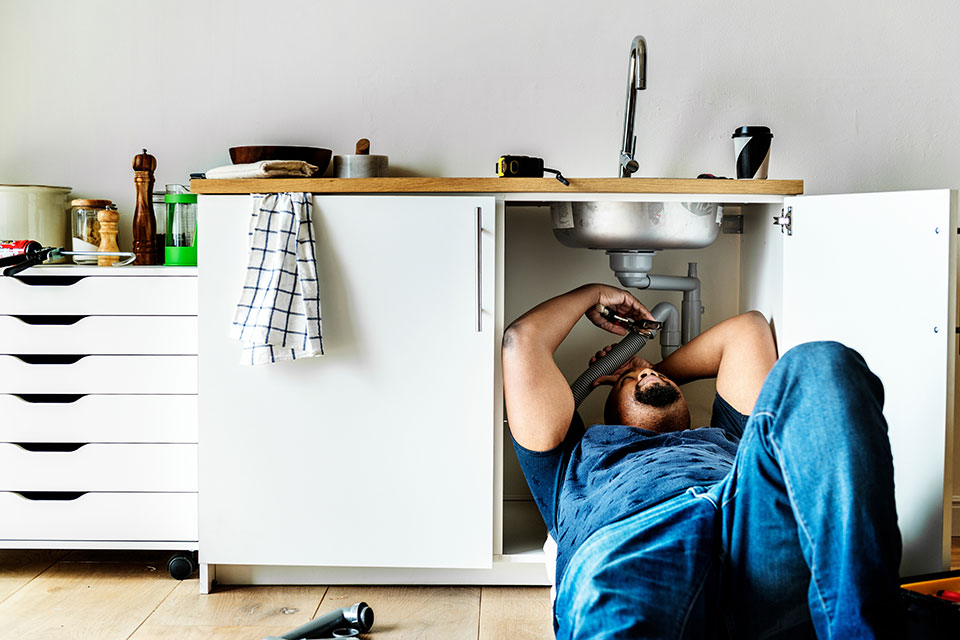 A plumber underneath a kitchen sink performing kitchen sink plumbing