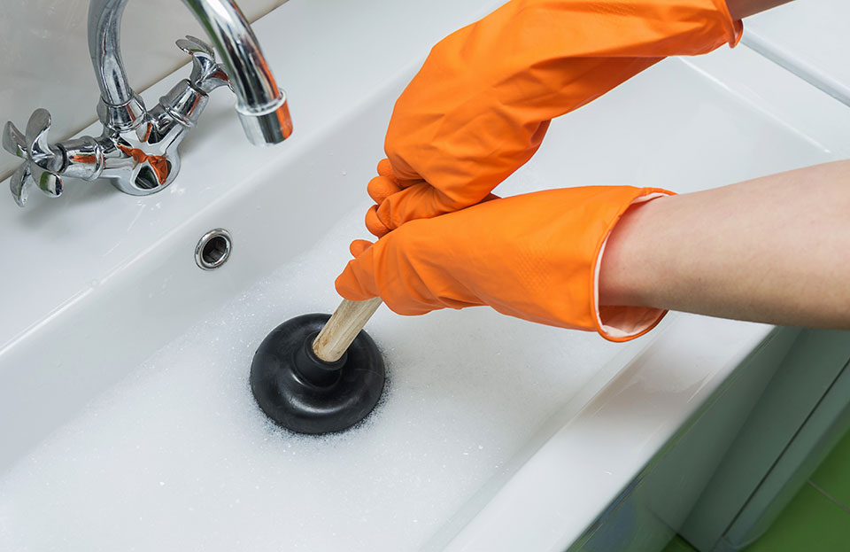 A plumber using a plunger on a sink drain to provide sink plumbing